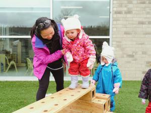educator helping a toddler climb a wooden obstacle